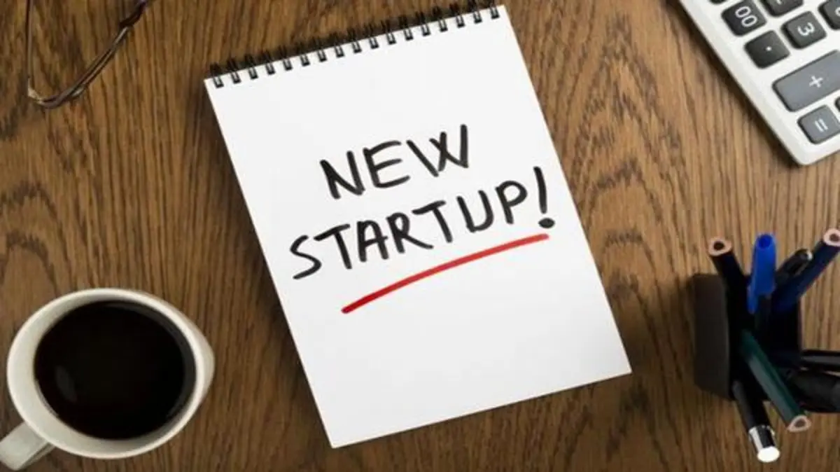 مكتب عمل عليه دفتر ملاحظات مكتوب عليه "NEW STARTUP!"، يمثل بداية مشروع ناشئ وأهم المهارات التي يحتاجها رائد الأعمال.