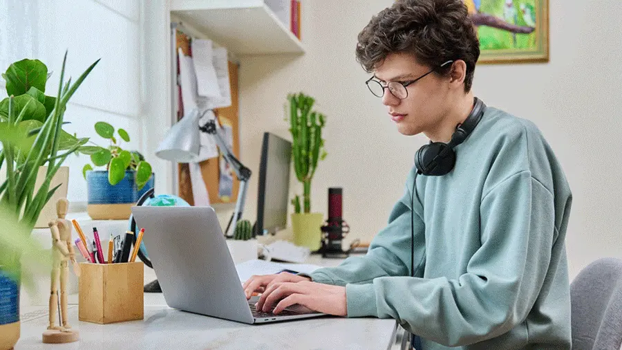 شاب يدرس تعليم عن بعد على حاسوب في منزله، يمثل الجانب النفسي والاجتماعي للدراسة عن بعد