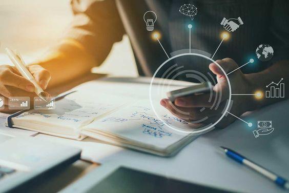 أيدي تعمل على دفتر ولابتوب مع أيقونات رقمية، تمثل رواد أعمال يخططون ويستخدمون التكنولوجيا لتطوير الأعمال.