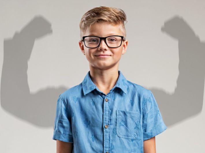 طفل يبتسم مع ظل أذرع قوية يمثل بناء شخصية قوية لدى الأطفال وتنمية قوتهم الكامنة